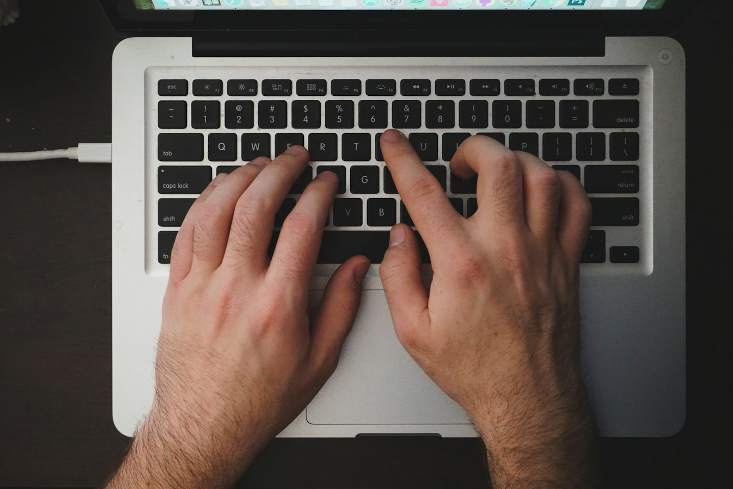 Tangan mengetik di keyboard laptop dengan layar terlihat.