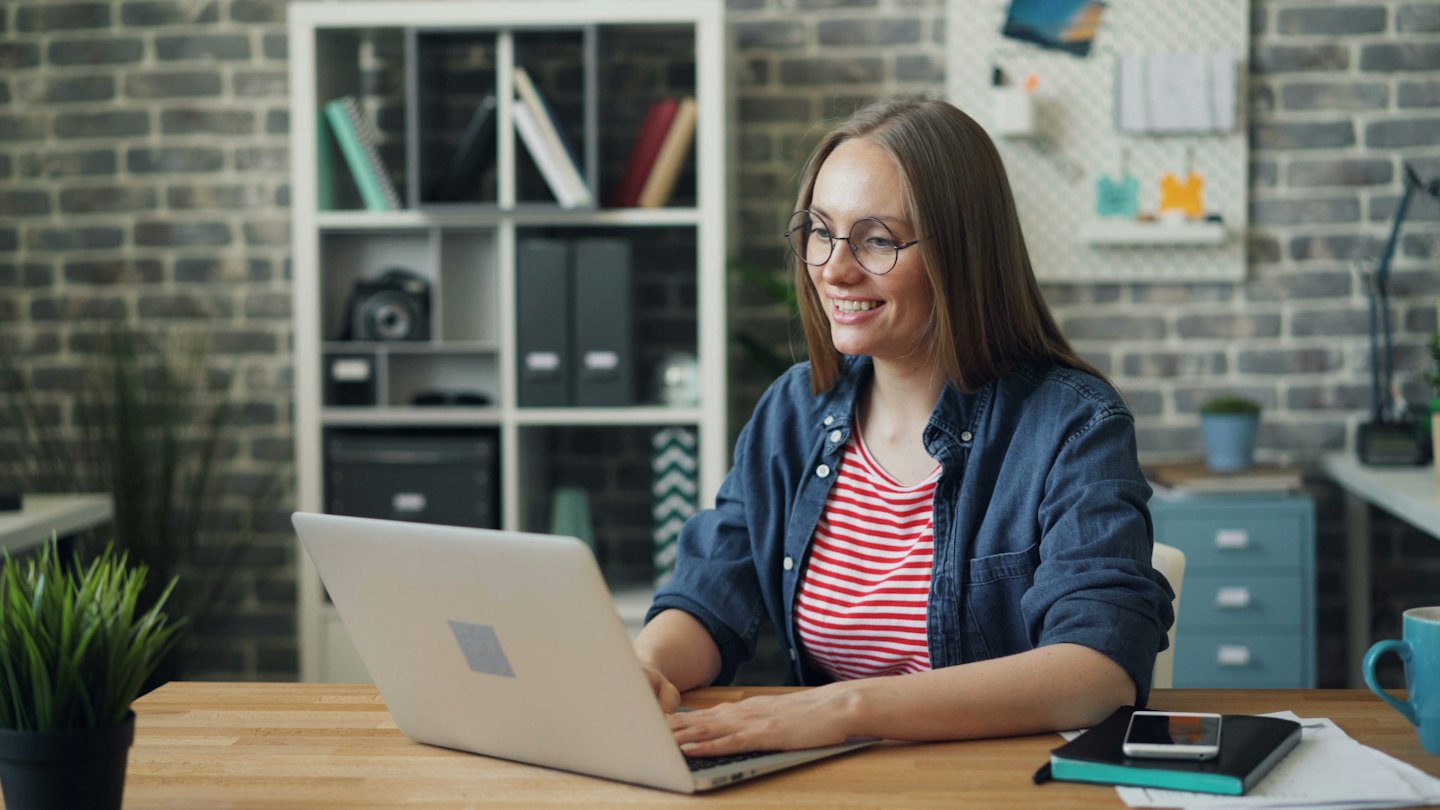 Wanita berkacamata mengetik di laptop di meja.